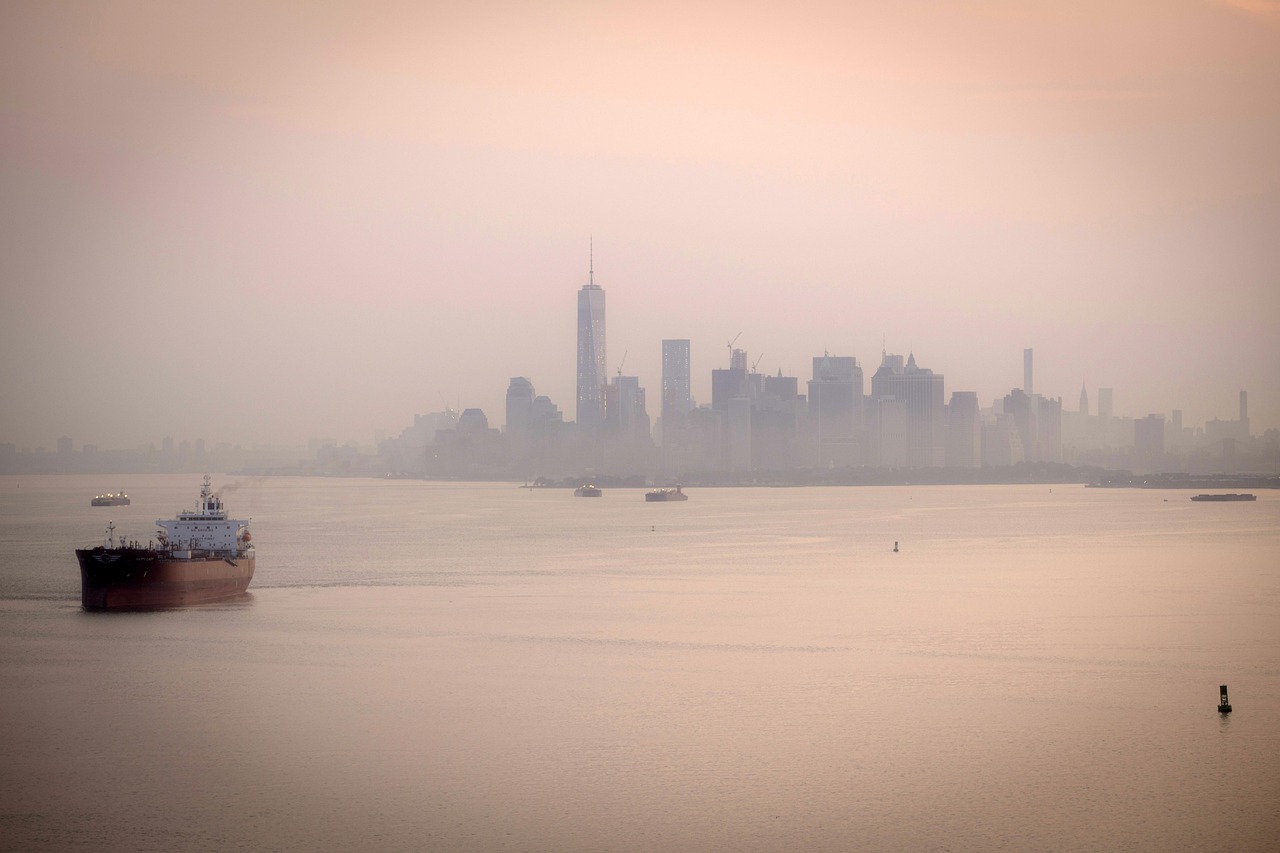 A misty view of a city skyline with a ship in the foreground on a body of water.