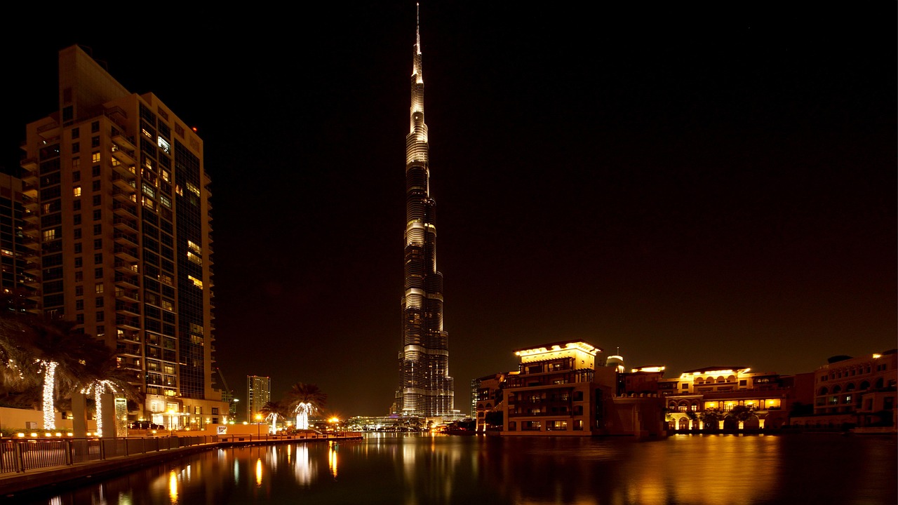 Night view of the Burj Khalifa and surrounding buildings reflected in the water in Dubai.