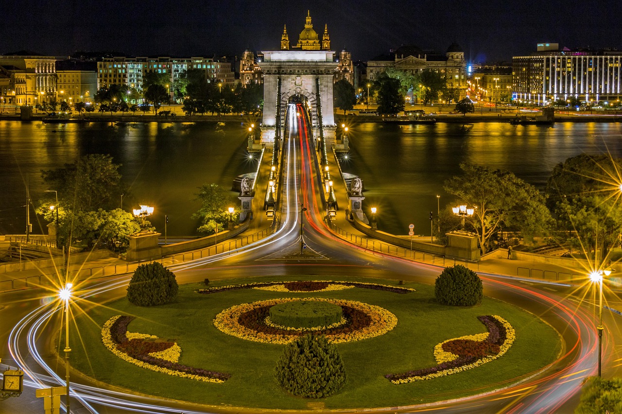 Night view of a city with a lit bridge over a river and a roundabout with flower arrangements in the shape of a heart.