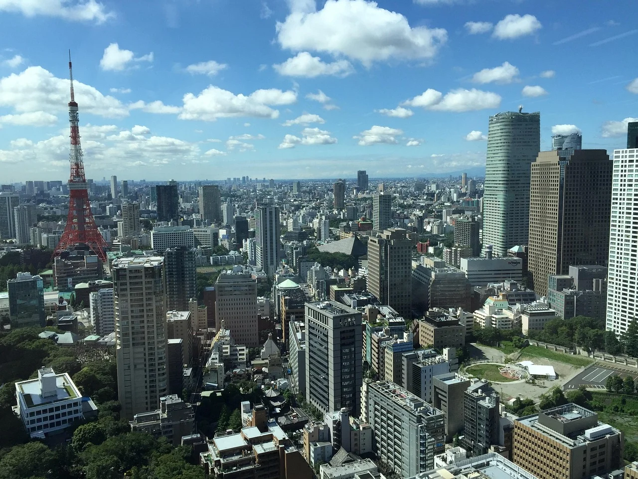 A panoramic view of a bustling city with tall buildings and a prominent red and white tower on the left.