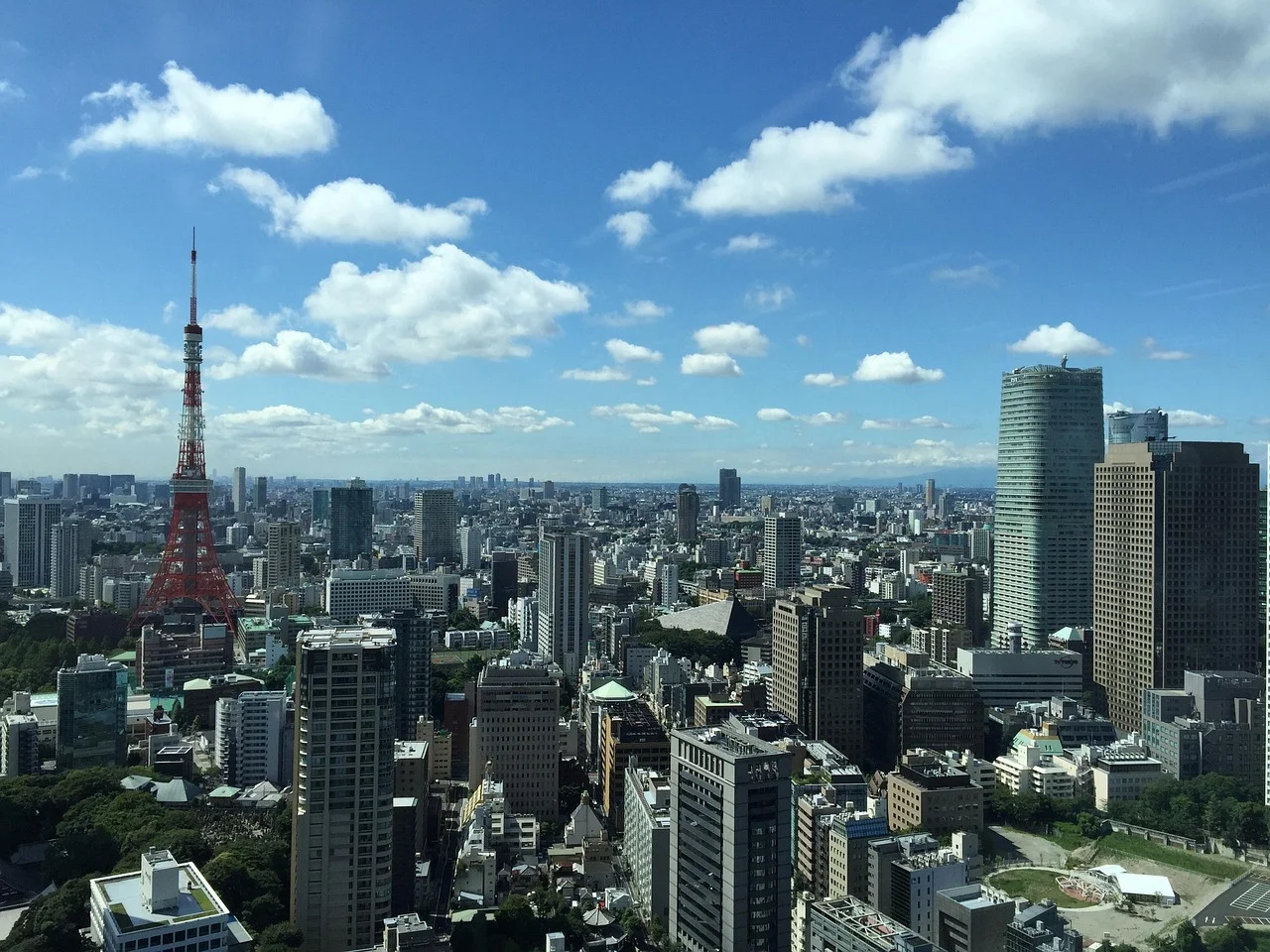 A panoramic view of a bustling city with tall buildings and a prominent red and white tower on the left.