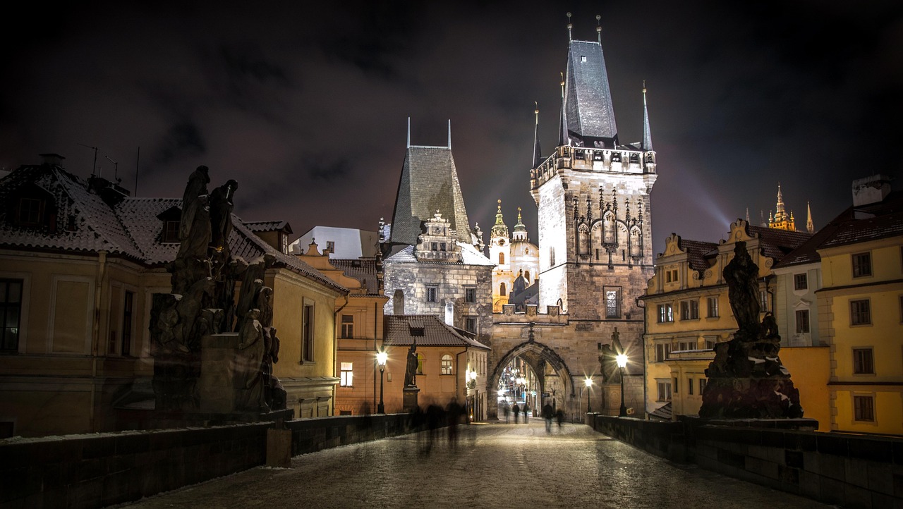 Night view of the Charles Bridge in Prague with statues and historic buildings illuminated.