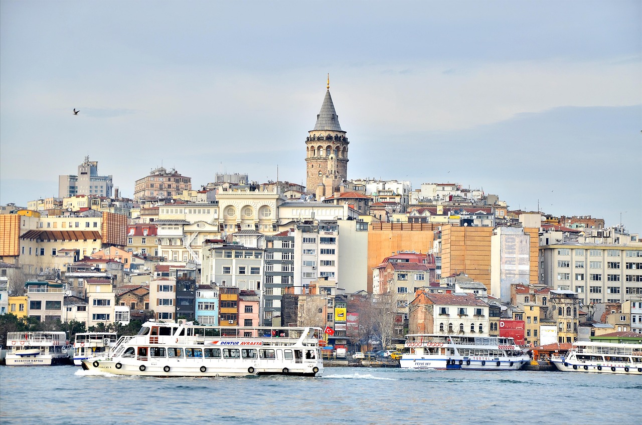A cityscape of Istanbul with boats on the water in the foreground and the Galata Tower prominently visible in the background.