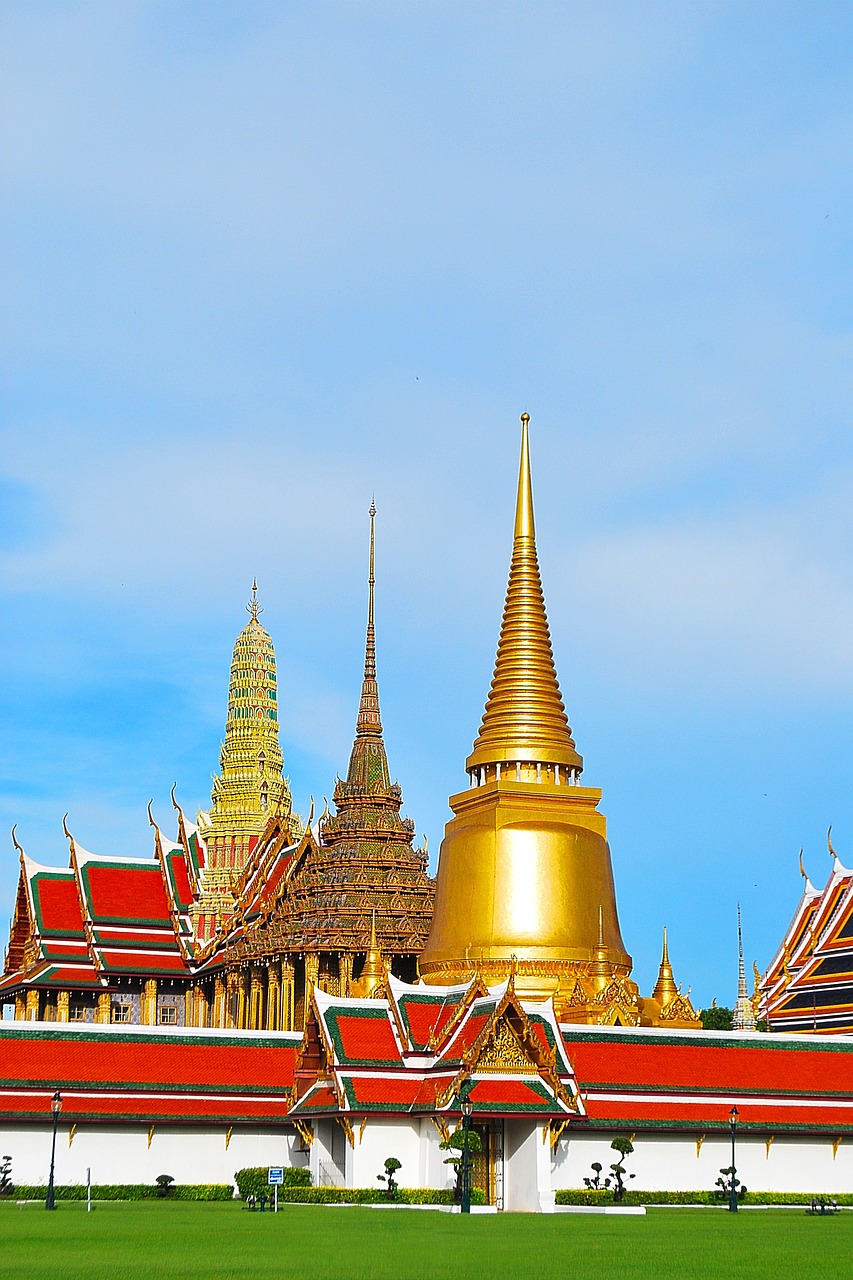 Golden temples and spires of the Grand Palace in Bangkok, Thailand, under a clear blue sky.