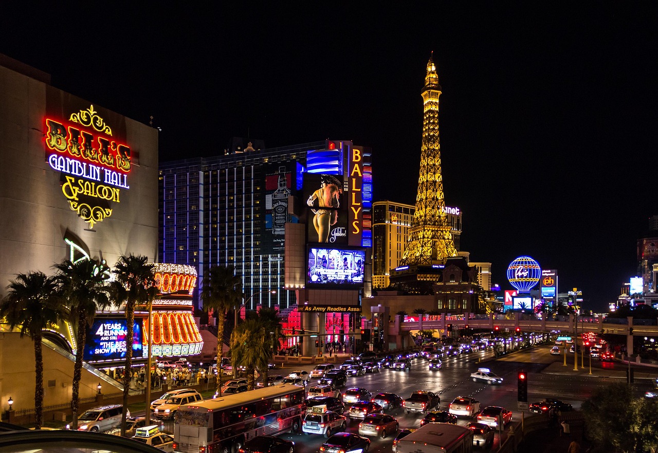 A bustling night scene in Las Vegas with bright neon signs, heavy traffic, and recognizable landmarks such as the Paris Las Vegas hotel with its Eiffel Tower replica.