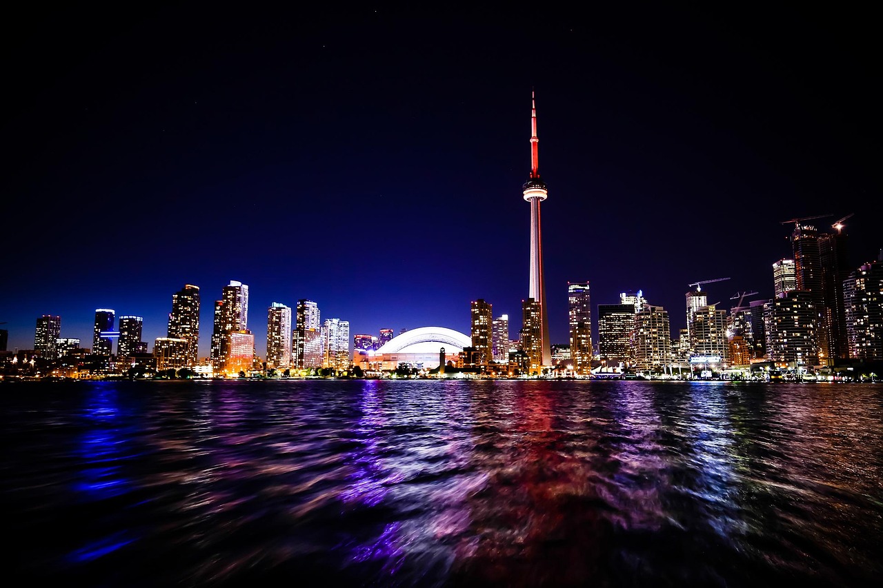Nighttime cityscape of Toronto with the CN Tower and other skyscrapers reflected in the water.