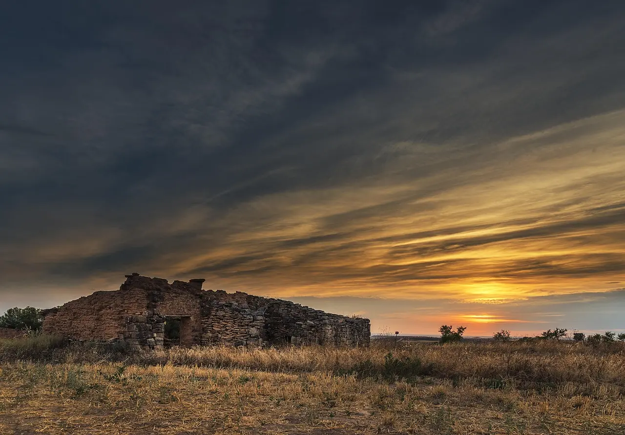An old, abandoned stone building at sunset in a rural, open field.