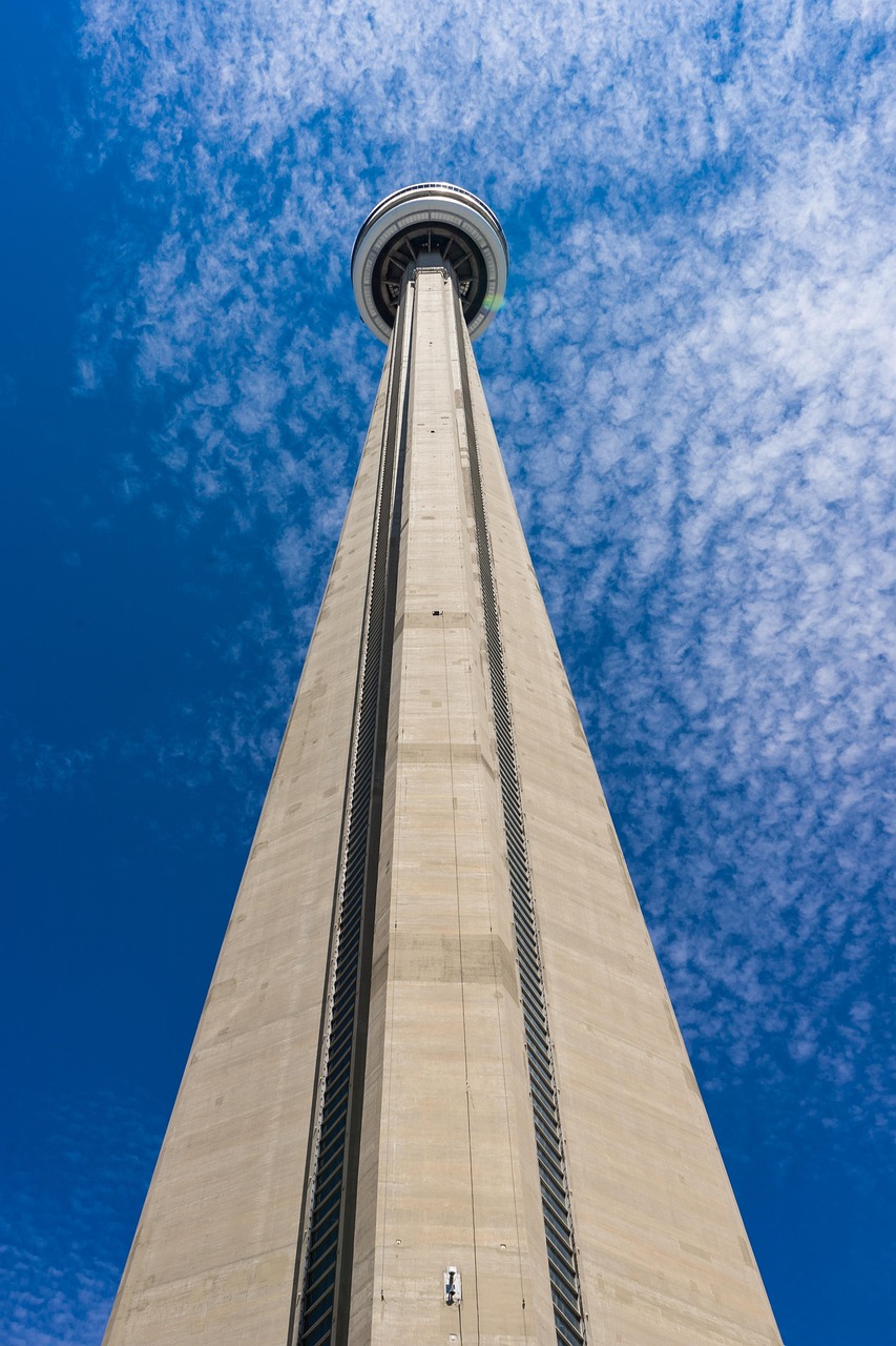 A tall tower with a circular observation deck at the top, viewed from a low angle against a blue sky with clouds.