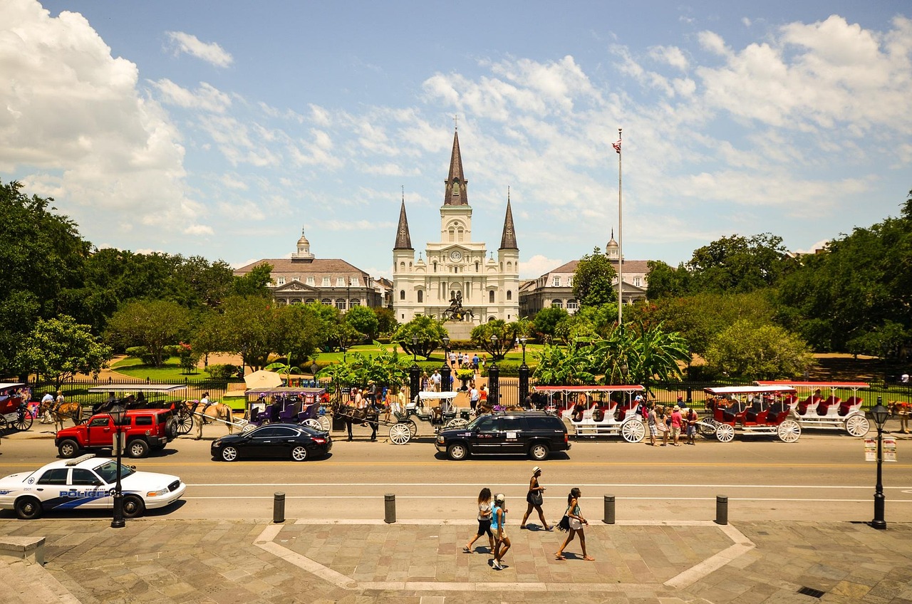 A bustling street scene in front of a large cathedral with horse-drawn carriages and various vehicles.