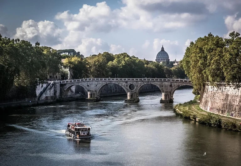 A boat on a river with a historic bridge and a dome in the background.