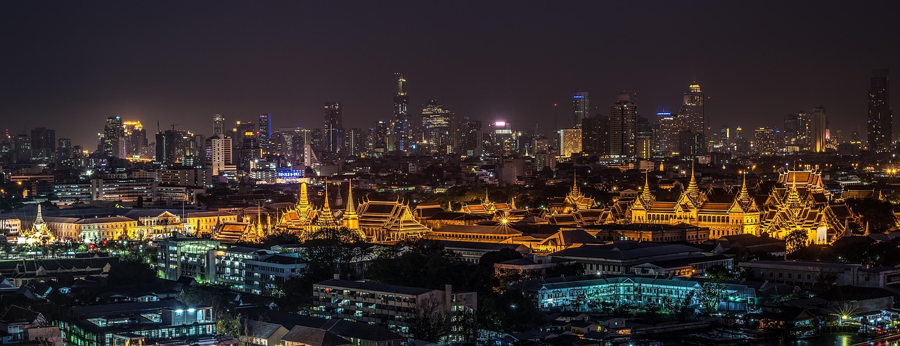 Nighttime cityscape of Bangkok with illuminated temples and modern skyscrapers.