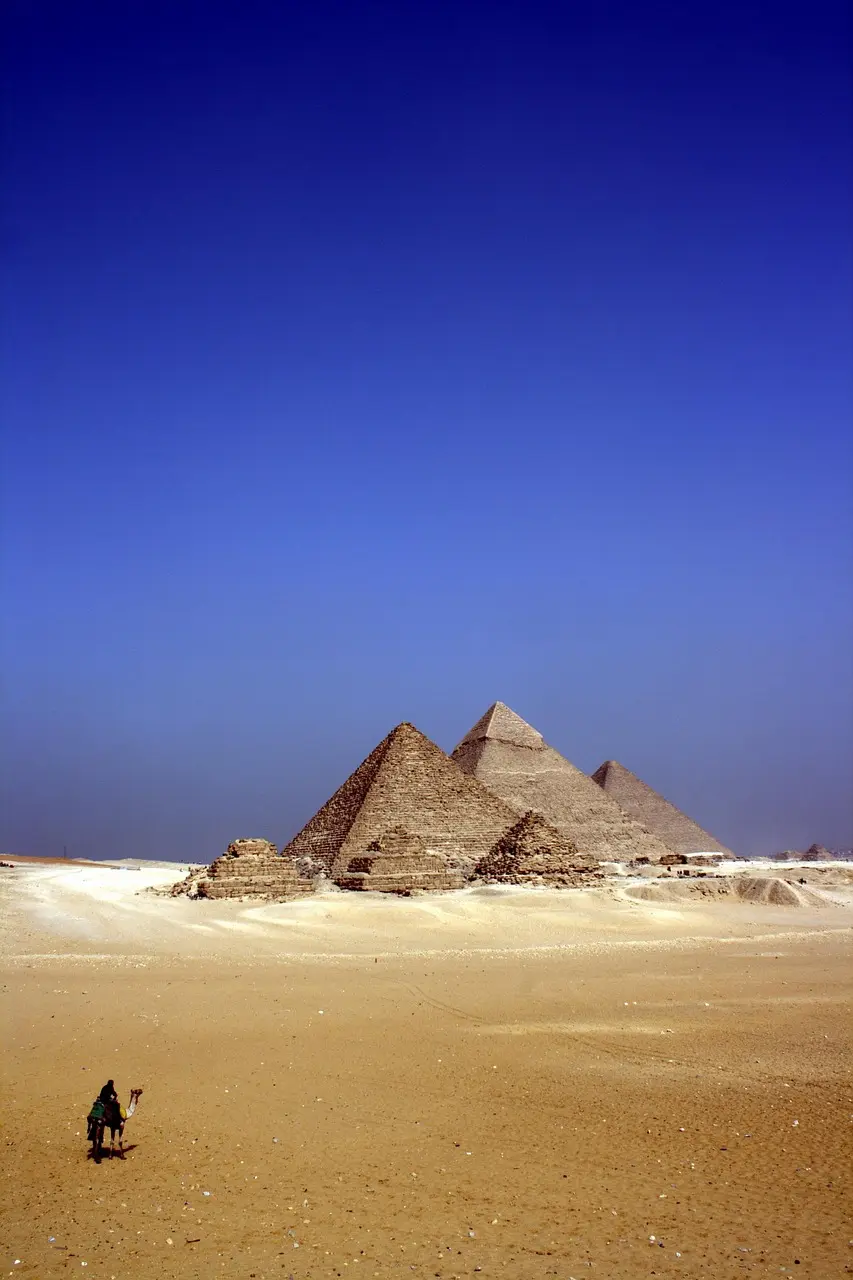 A person riding a camel in front of the pyramids in a desert landscape.