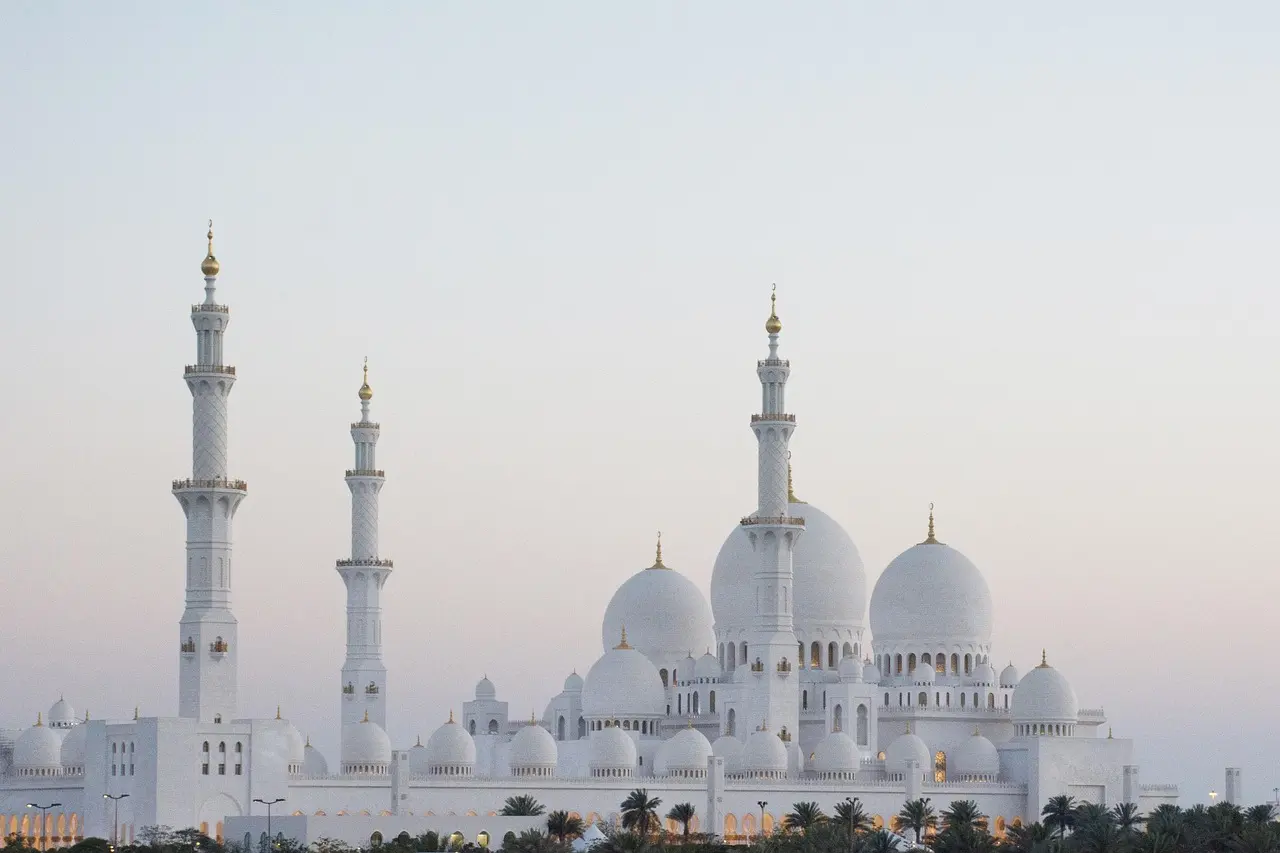 A grand white mosque with multiple domes and minarets under a clear sky.