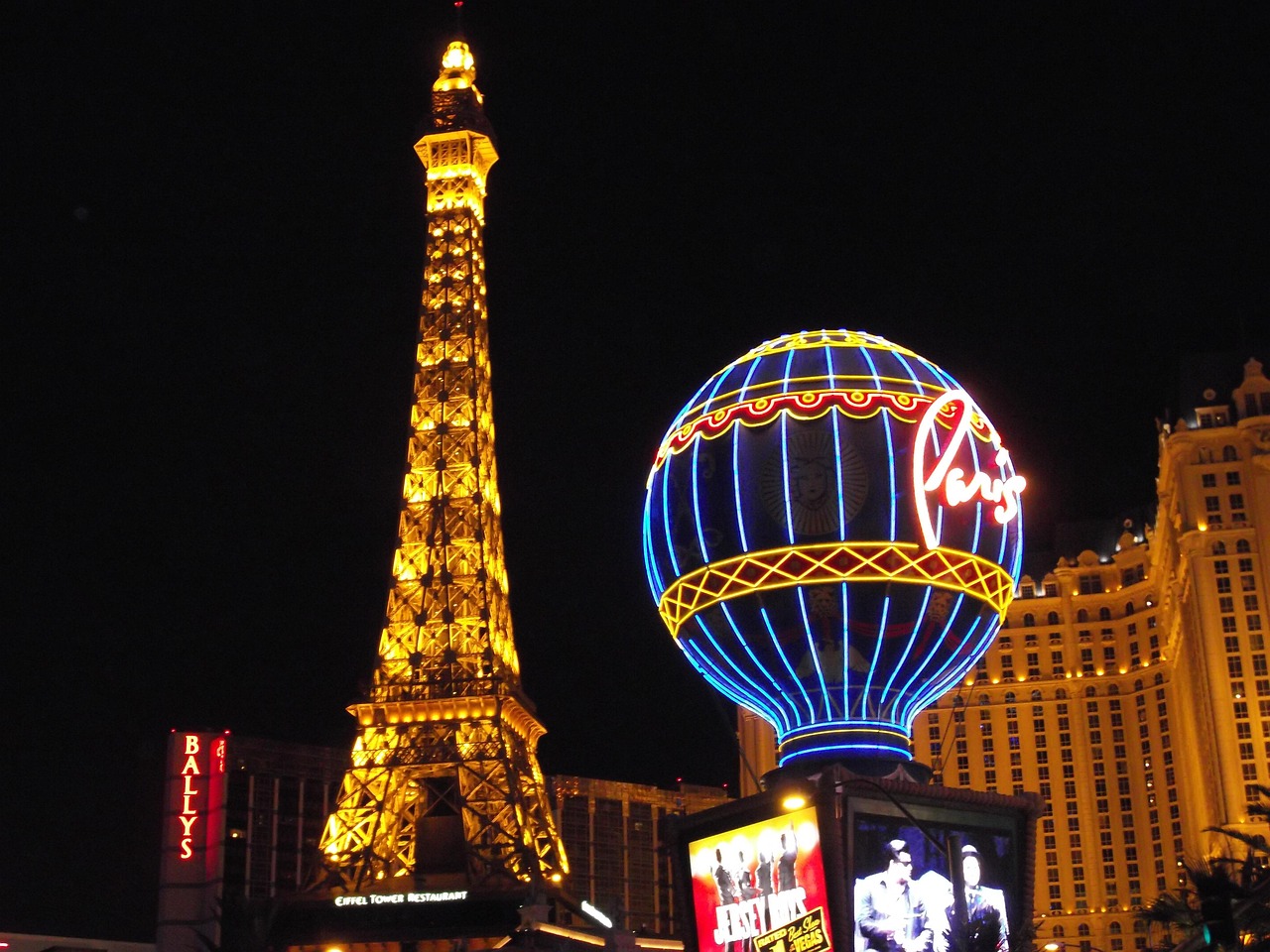 A night view of the Paris Las Vegas hotel with a replica Eiffel Tower and a neon hot air balloon sign.