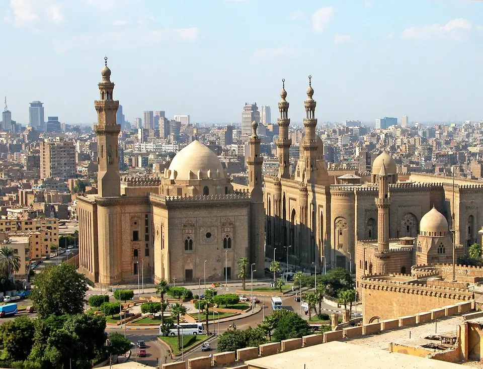 A large historical mosque with multiple minarets and domes in an urban cityscape.
