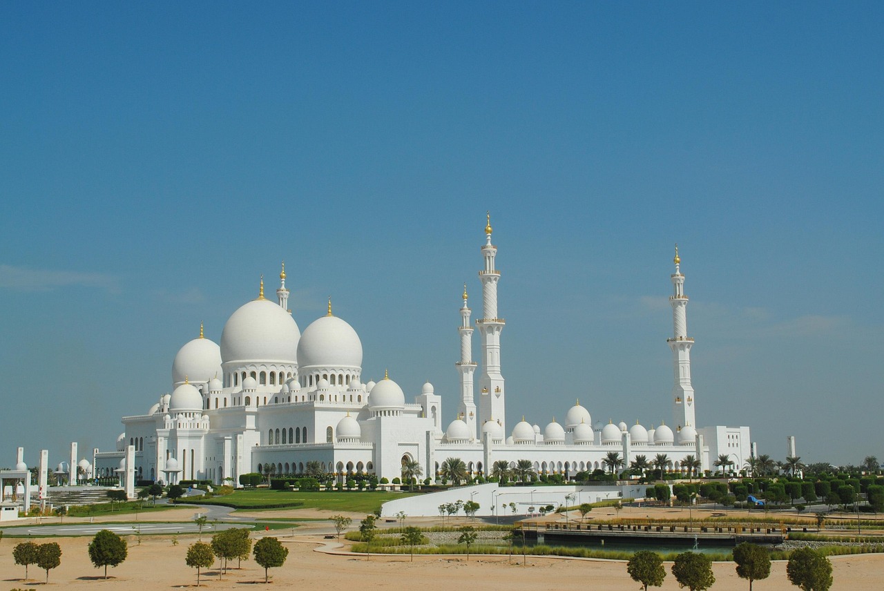 A large white mosque with multiple domes and minarets under a clear blue sky.
