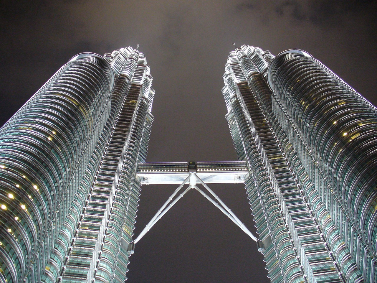 Two tall, curved skyscrapers with a skybridge connecting them, viewed from a low angle at night.