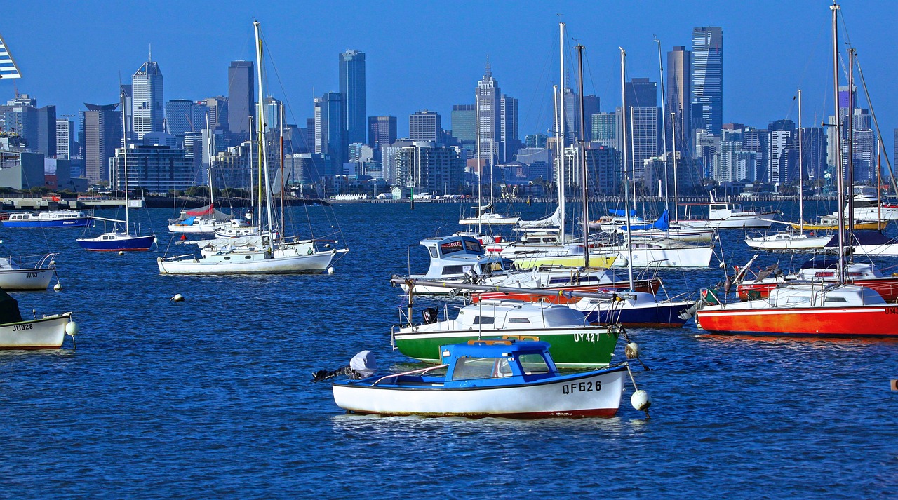 A harbor with various boats and a city skyline in the background.