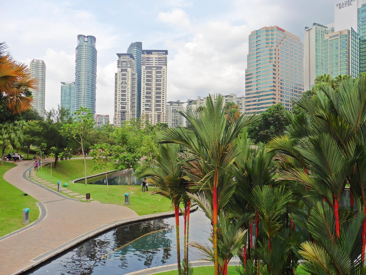 A city park with palm trees and a water feature, surrounded by tall skyscrapers.