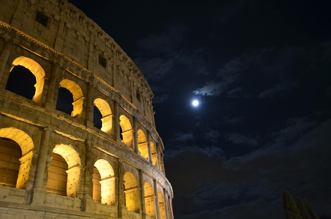 The Colosseum in Rome, Italy, illuminated at night with a full moon in the sky.
