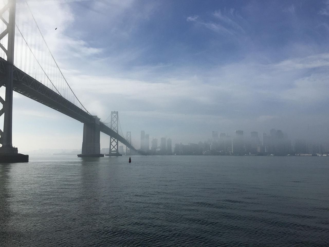 A foggy view of a city skyline with a large suspension bridge in the foreground.