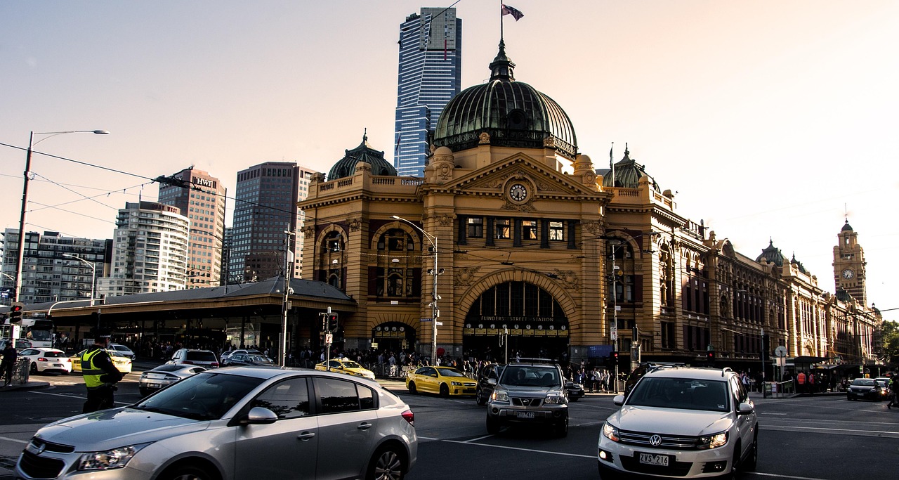 A bustling city street in front of a historic train station with modern skyscrapers in the background.