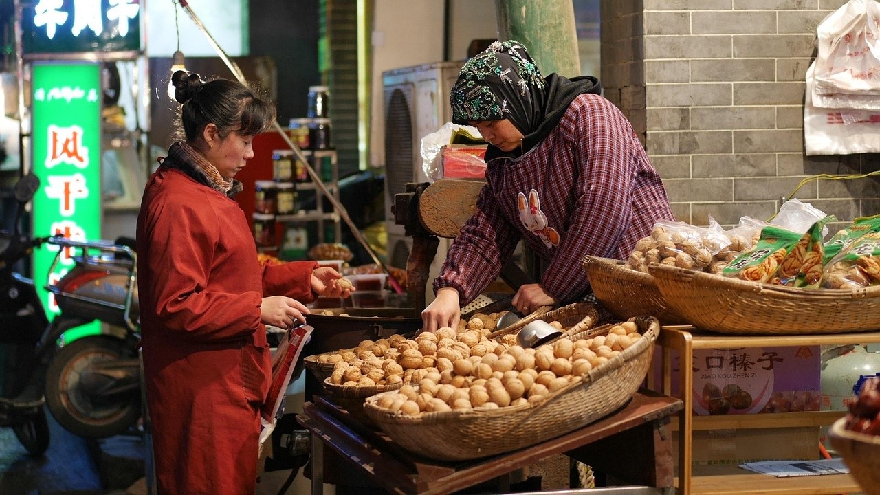 Two women in a night market, one selling food from a basket.