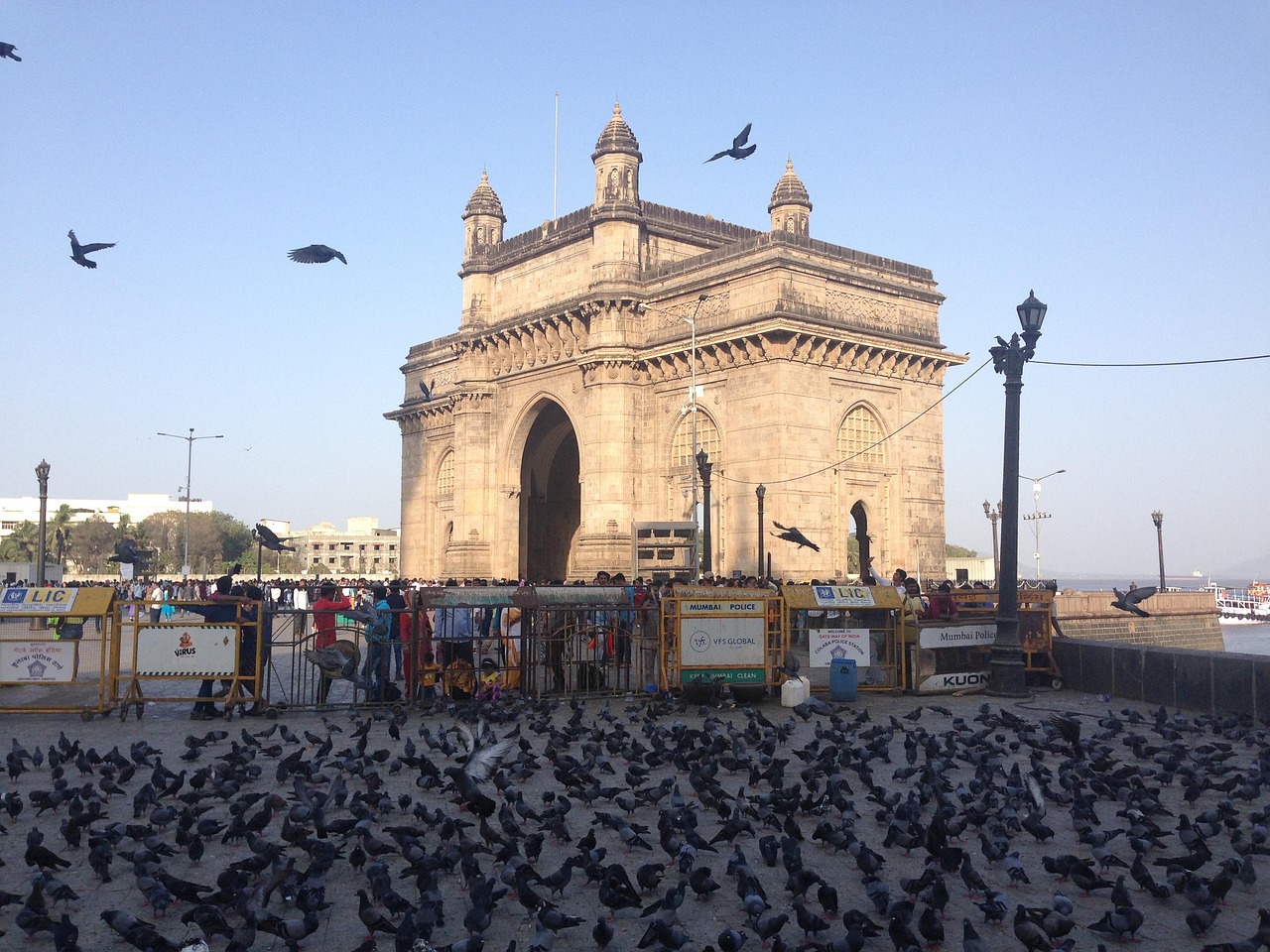 A large crowd of people and pigeons in front of the Gateway of India in Mumbai, India.