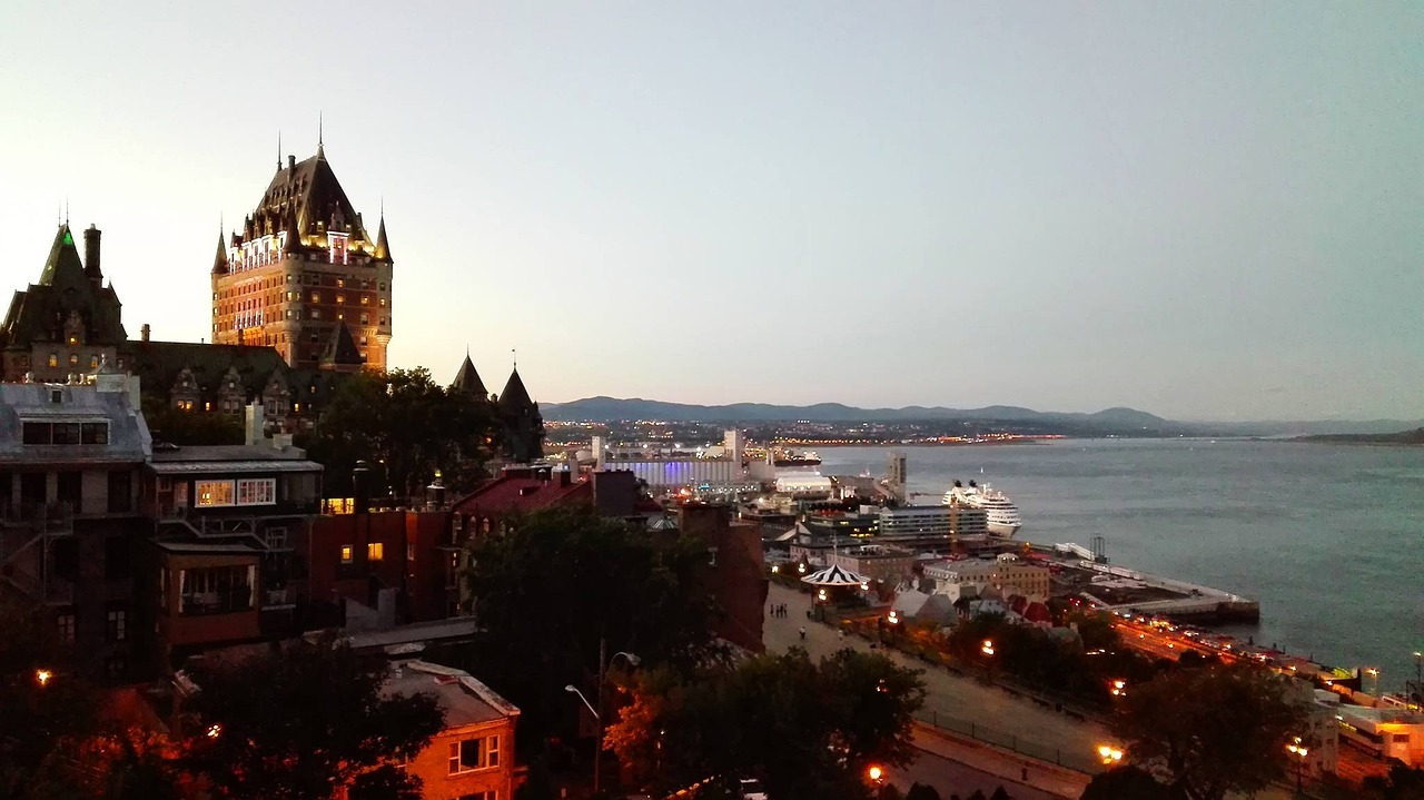 Evening view of Quebec City with the Chateau Frontenac prominently lit, overlooking the St. Lawrence River with a cruise ship docked nearby.