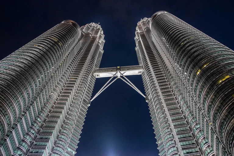 Two tall skyscrapers connected by a skybridge at night.