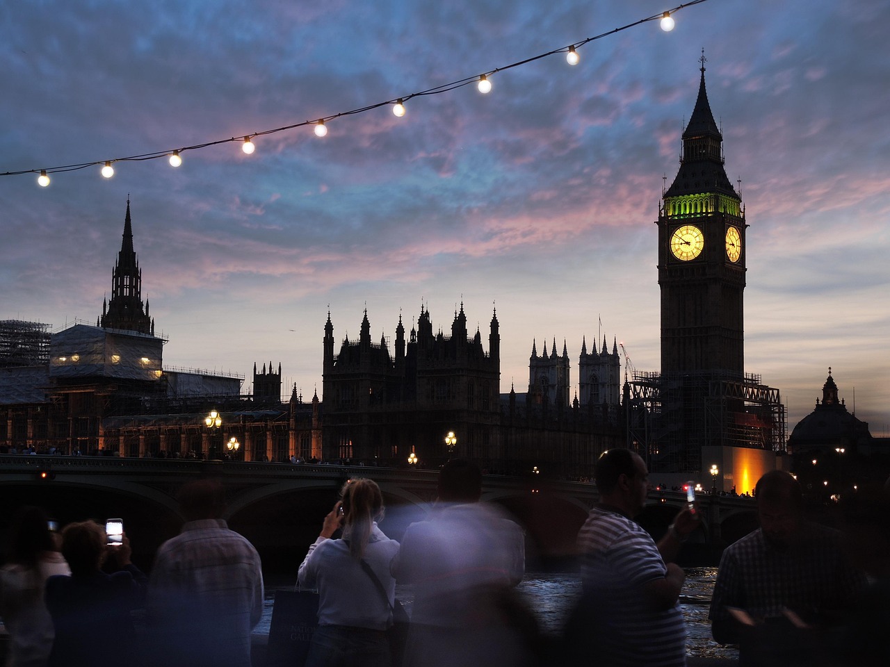 A group of people taking photos of the Palace of Westminster and Big Ben at dusk.
