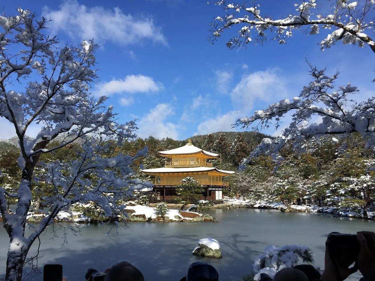 A golden pavilion surrounded by snow-covered trees and a pond in a serene landscape.