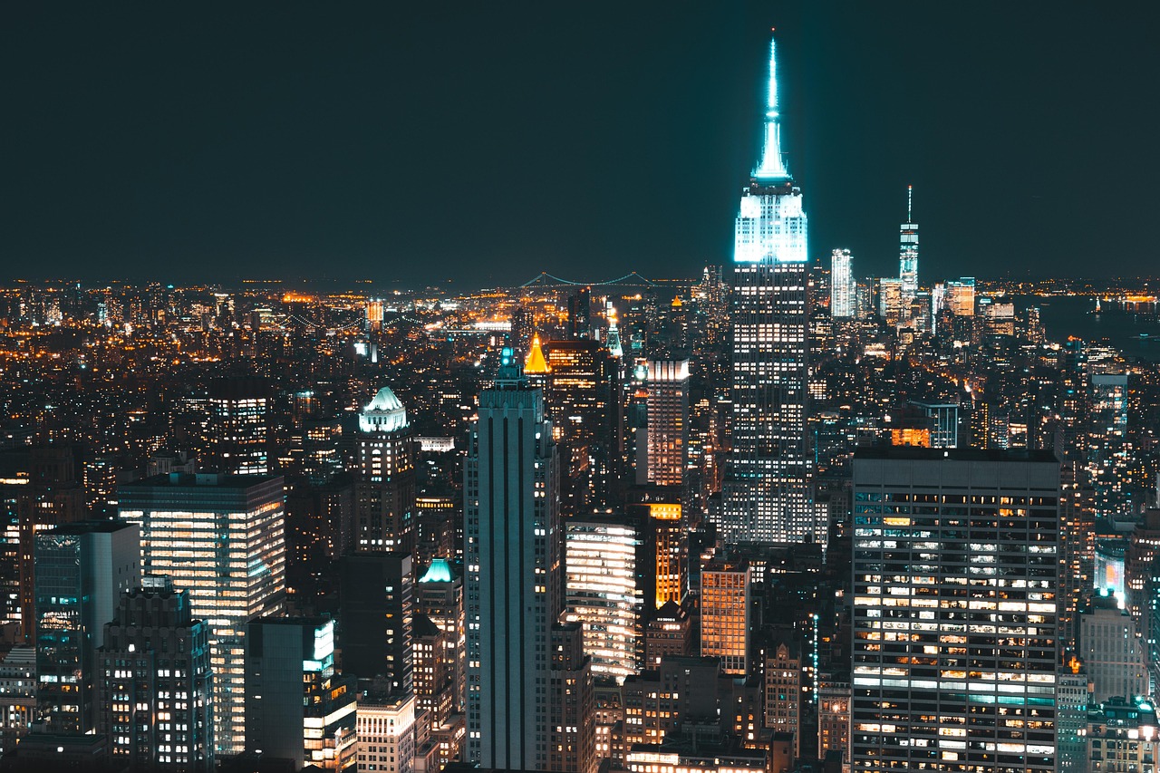 Nighttime cityscape of New York with illuminated skyscrapers, including the Empire State Building.