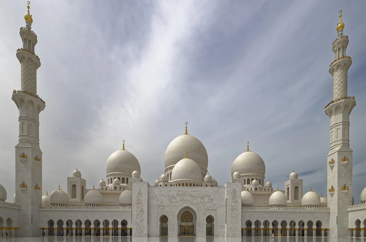 A grand mosque with multiple domes and minarets under a cloudy sky.