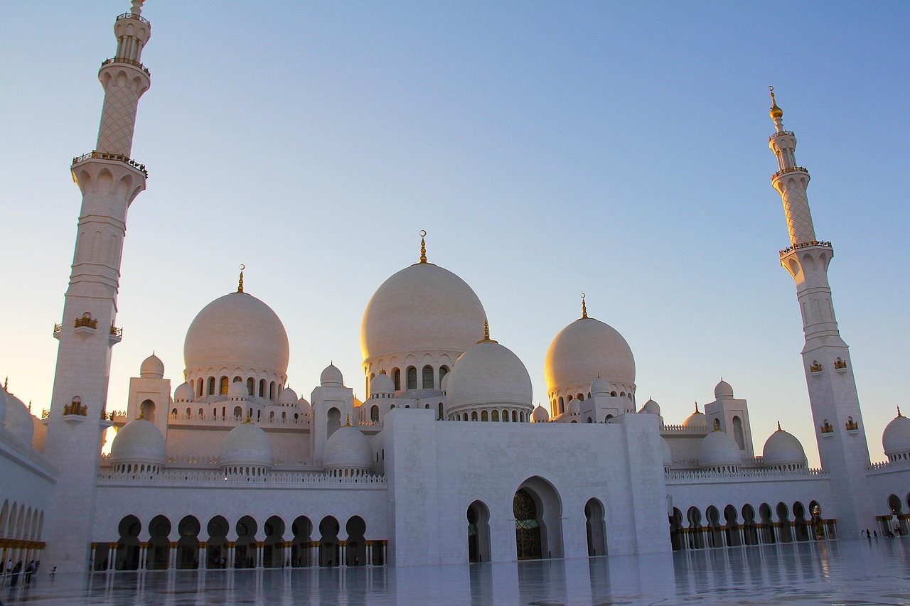 A grand mosque with large white domes and tall minarets at sunset.