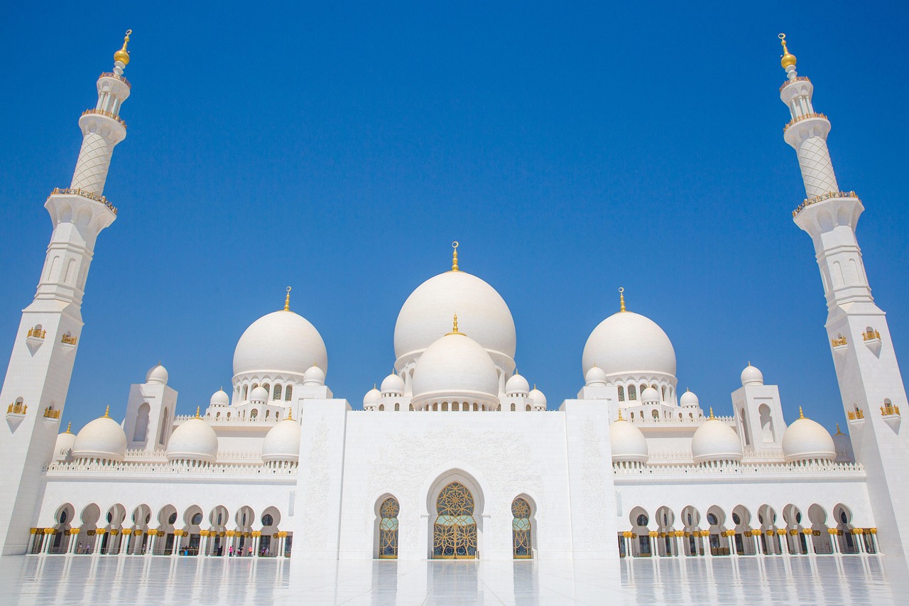 A grand white mosque with multiple domes and minarets under a clear blue sky.