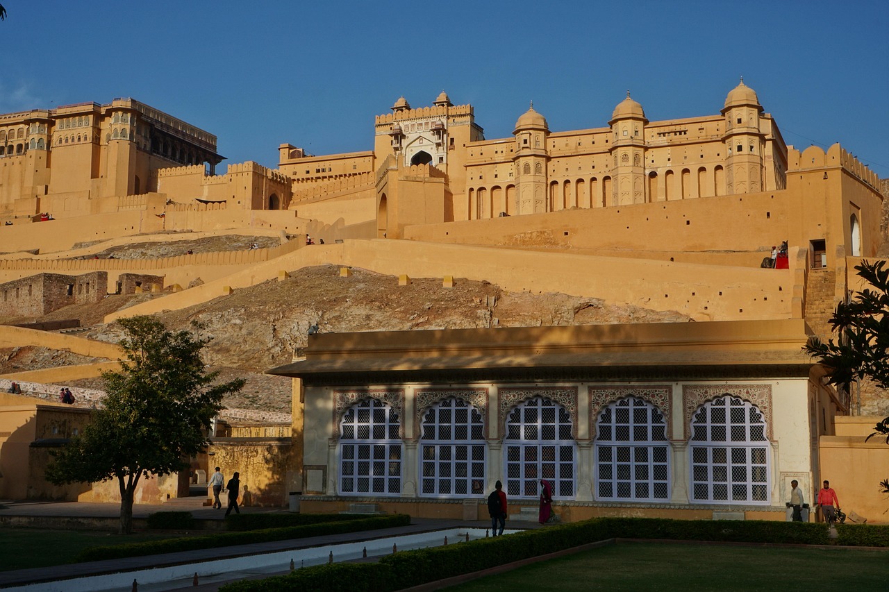 A grand historical fort with intricate architecture, set against a clear blue sky, with people walking around the grounds.
