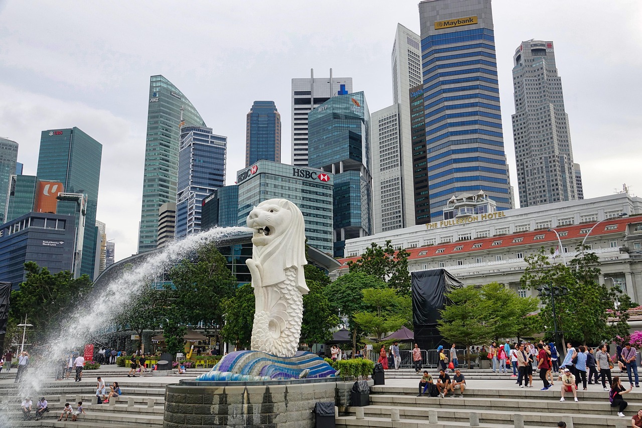 A large Merlion statue spouting water in front of a bustling cityscape with tall buildings and people in the foreground.