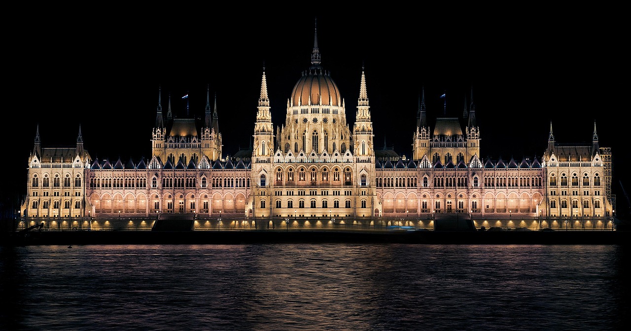 A grand, illuminated building with a large dome and multiple spires, reflected in the water in front of it at night.