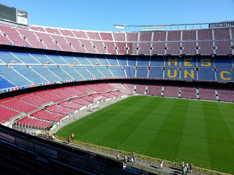 A large stadium with a green soccer field and tiered seating in various colors.