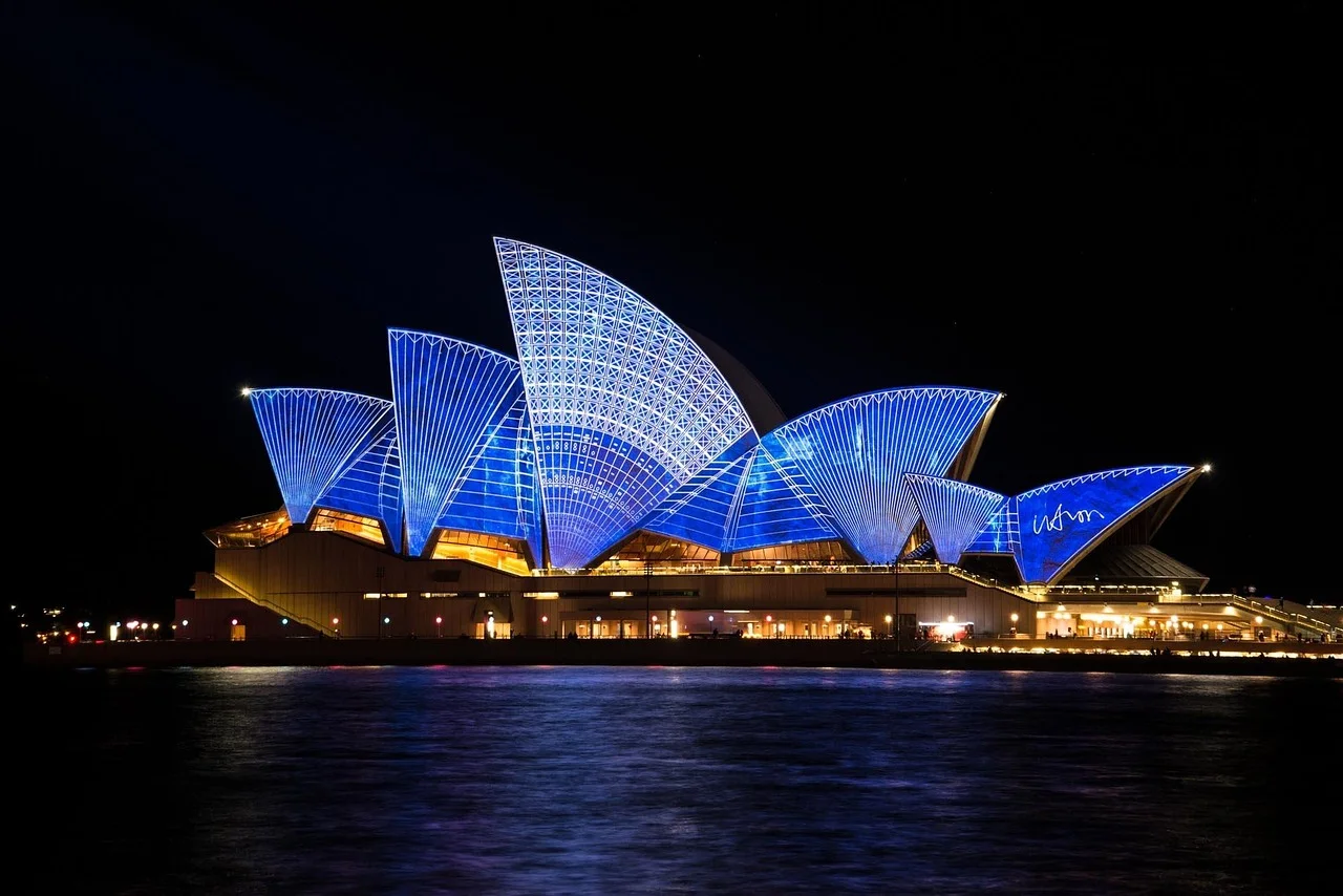 Sydney Opera House illuminated at night with blue lights reflecting on the water.