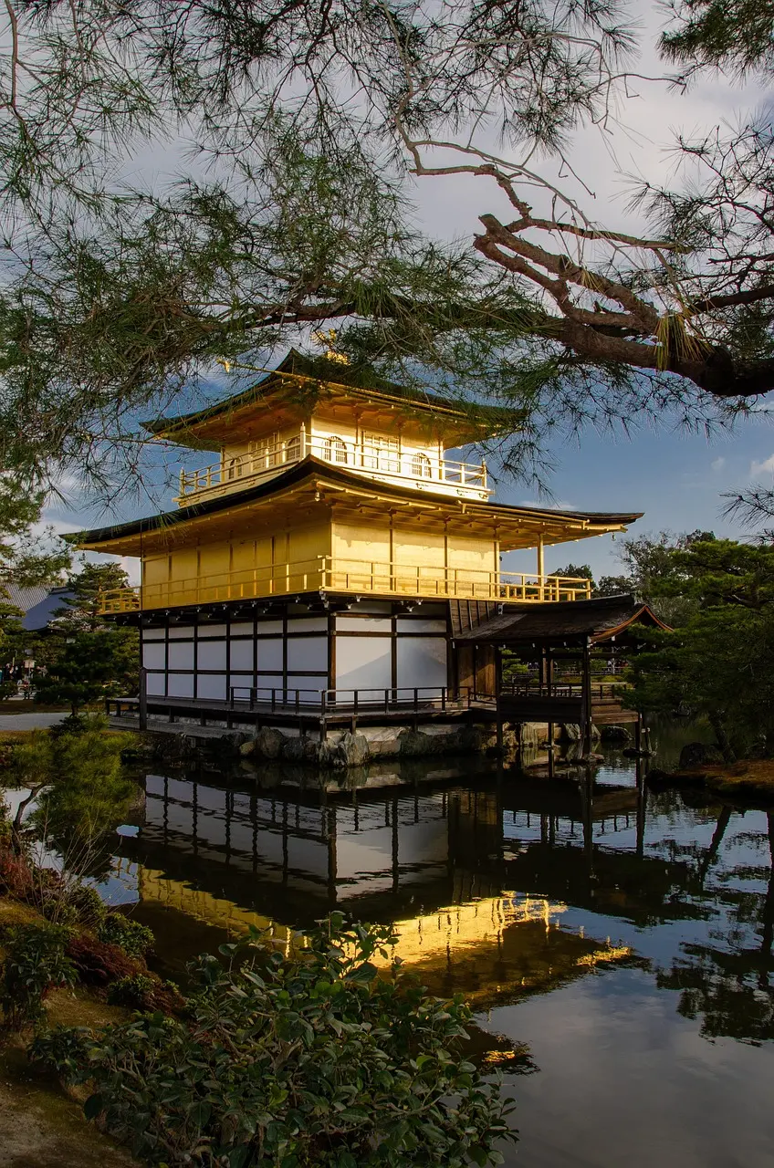 A golden pavilion reflected in a calm pond surrounded by greenery.