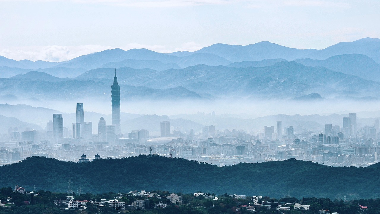 A misty cityscape with a prominent tall tower and surrounding buildings, set against a backdrop of mountains.