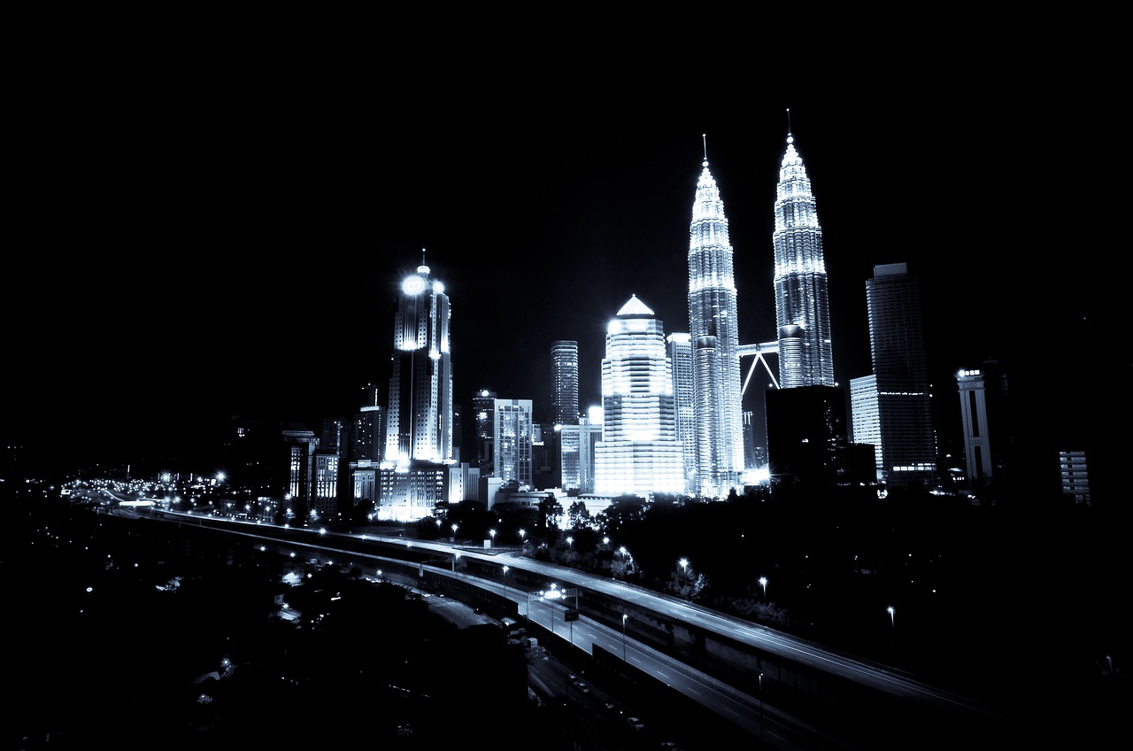 Night view of a city skyline with tall illuminated skyscrapers and a highway in the foreground.