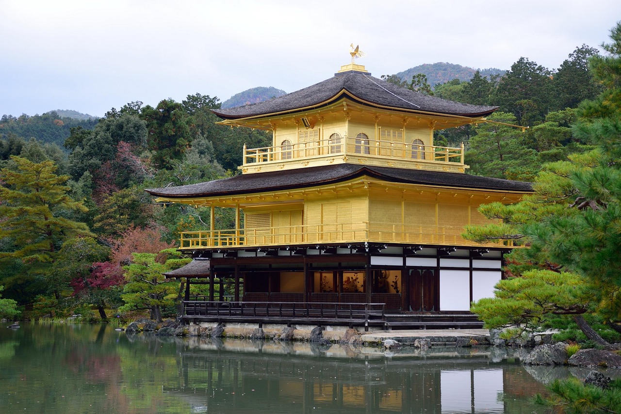 A golden pavilion reflecting in a calm body of water surrounded by lush greenery.