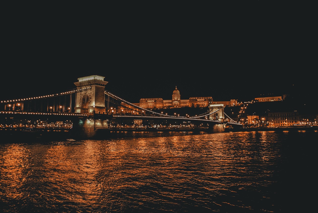 A night view of the Chain Bridge and the Buda Castle in Budapest, Hungary, with the river reflecting the lights.