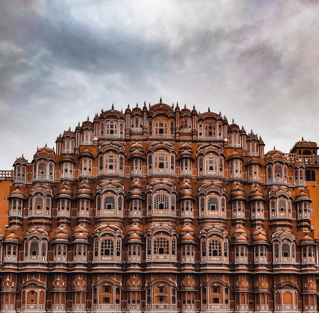 A detailed view of the Hawa Mahal palace in Jaipur, India, showcasing its intricate red and pink sandstone latticework and windows.