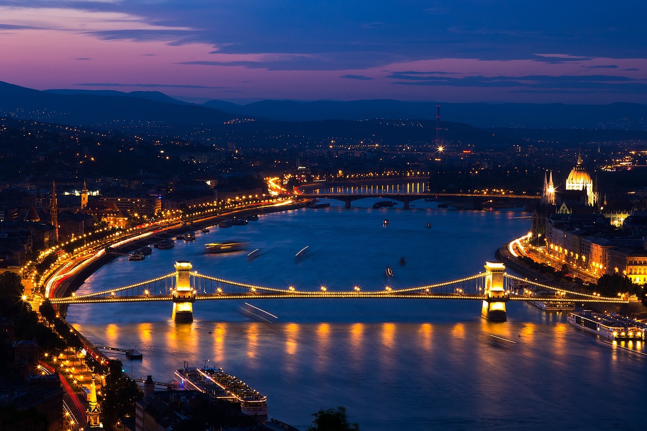 A nighttime view of a city with a lit bridge over a river, showing urban lights and a distant skyline.