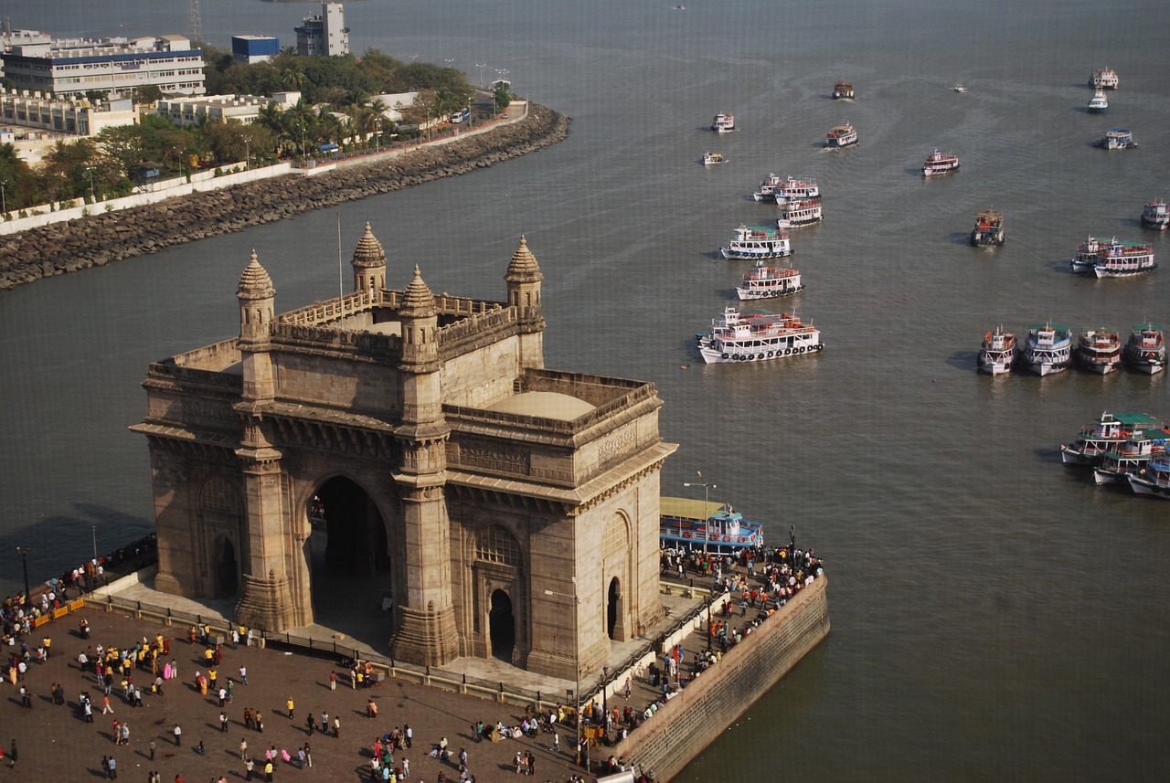 Aerial view of the Gateway of India in Mumbai with boats in the water and people gathered around.