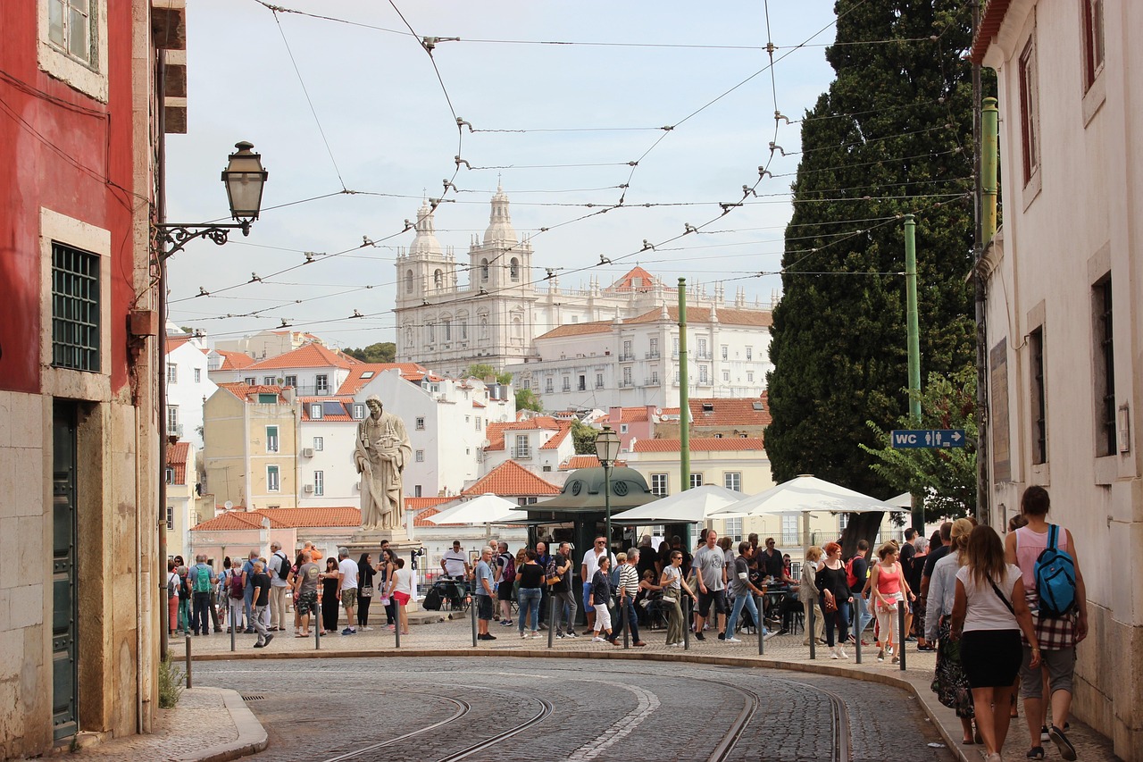 A bustling street in Lisbon, Portugal, with tourists and a view of the Jerónimos Monastery in the background.